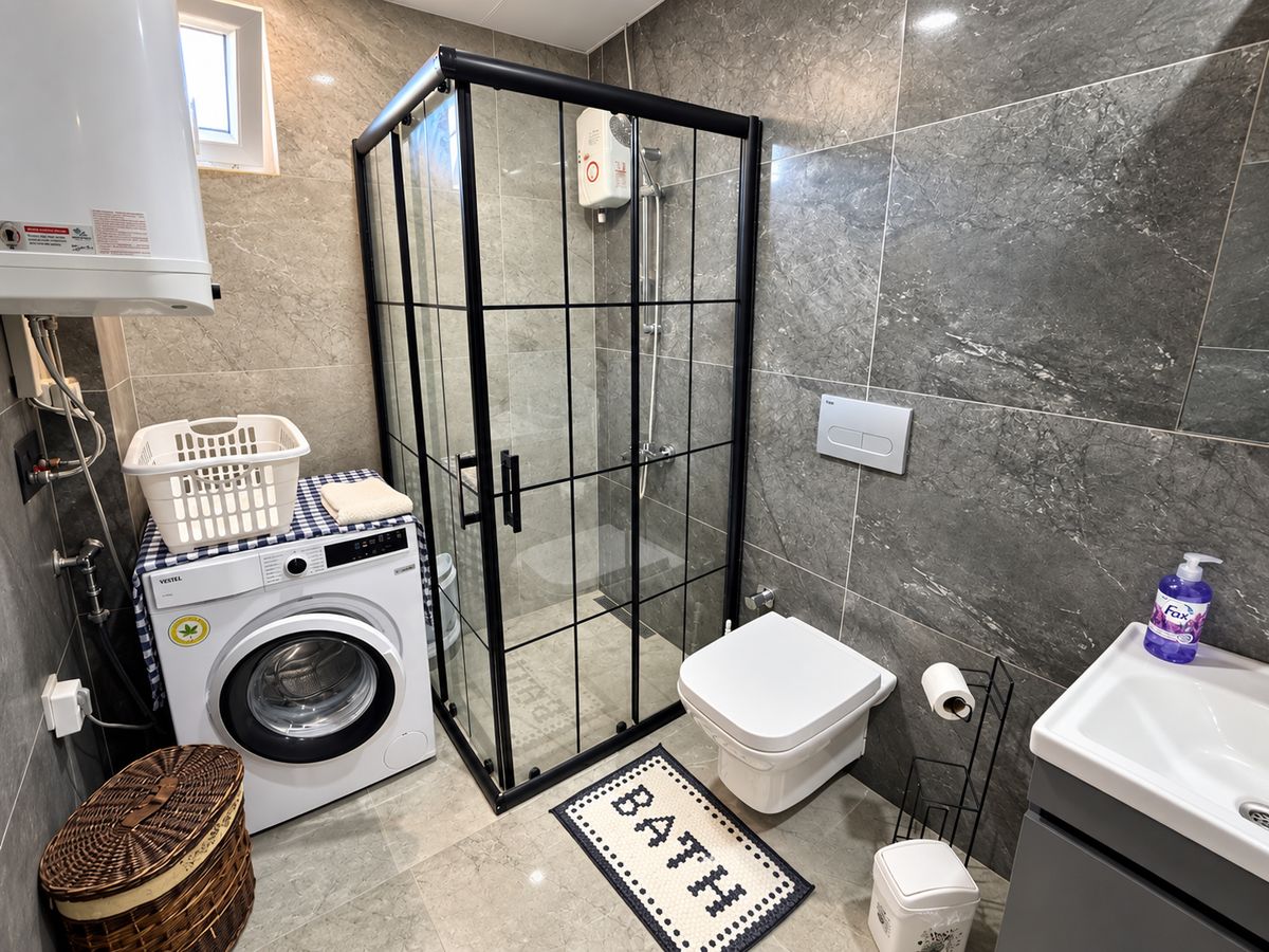 Bathroom with grey tiles, glass shower and washing machine